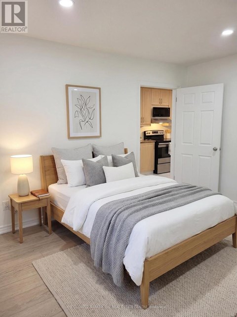A bedroom with a large bed, a nightstand with a lamp, and a framed picture on the wall.