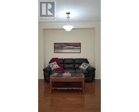 A black leather couch with pillows and a coffee table in front of a painting.
