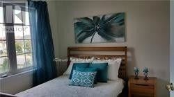 A bedroom with a bed, nightstand, and a painting of a palm tree on the wall.