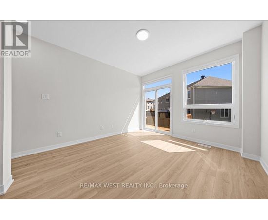 A spacious room with wooden flooring and white walls, with a window showing a view of a house.