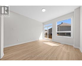 A spacious room with wooden flooring and white walls, with a window showing a view of a house.