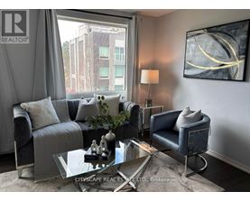 A living room with a grey couch, a glass coffee table, and a large window with a view of a building outside.