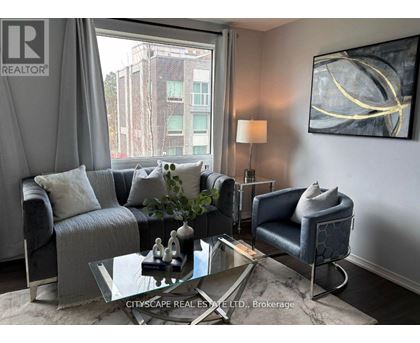 A living room with a grey couch, a glass coffee table, and a large window with a view of a building outside.