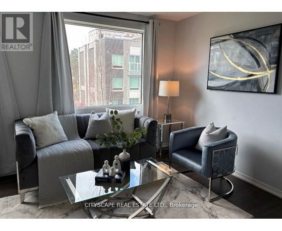 A living room with a grey couch, a glass coffee table, and a large window with a view of a building outside.