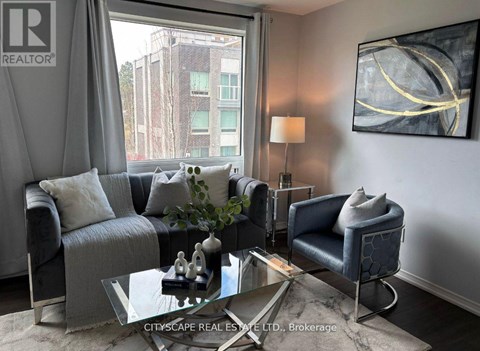 A living room with a grey couch, a glass coffee table, and a large window with a view of a building outside.