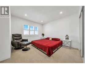 A bedroom with a red bed, a brown leather chair, and a small table with a vase on it.