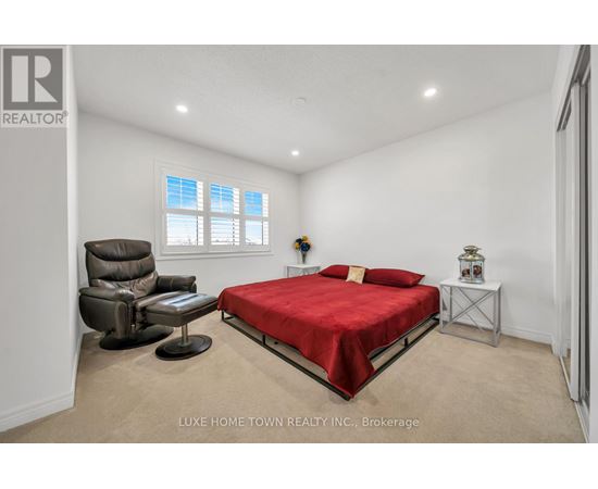 A bedroom with a red bed, a brown leather chair, and a small table with a vase on it.