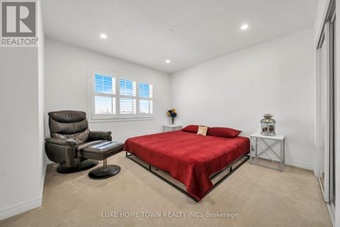 A bedroom with a red bed, a brown leather chair, and a small table with a vase on it.