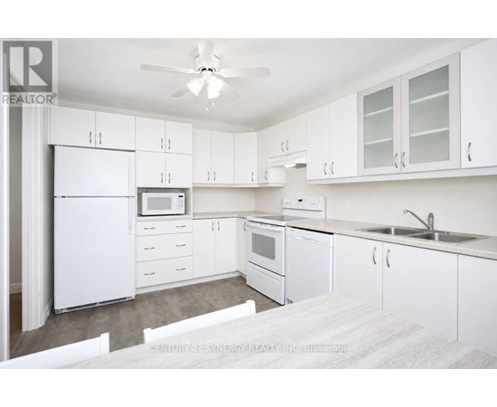 A white kitchen with a refrigerator, microwave, oven, sink, and cabinets.