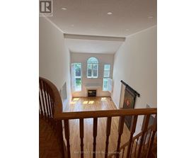 A view from the top of a staircase looking down at a living room with a fireplace and a bay window.