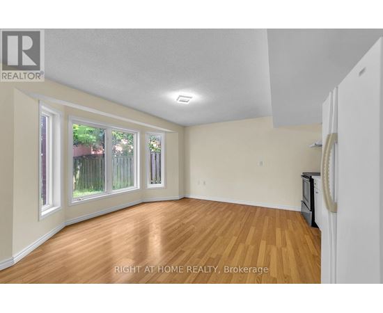 A room with wooden floors and white walls, with a window showing a fence and trees outside.