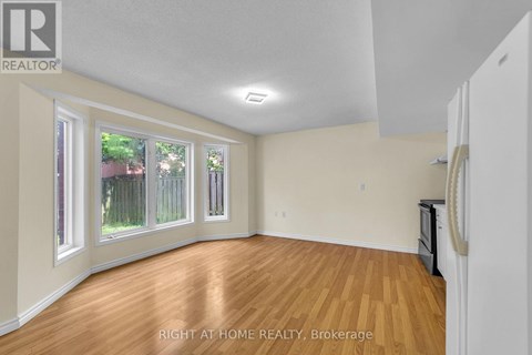A room with wooden floors and white walls, with a window showing a fence and trees outside.