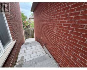 A red brick wall with a window on the left and a wooden fence in the background.