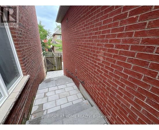A red brick wall with a window on the left and a wooden fence in the background.