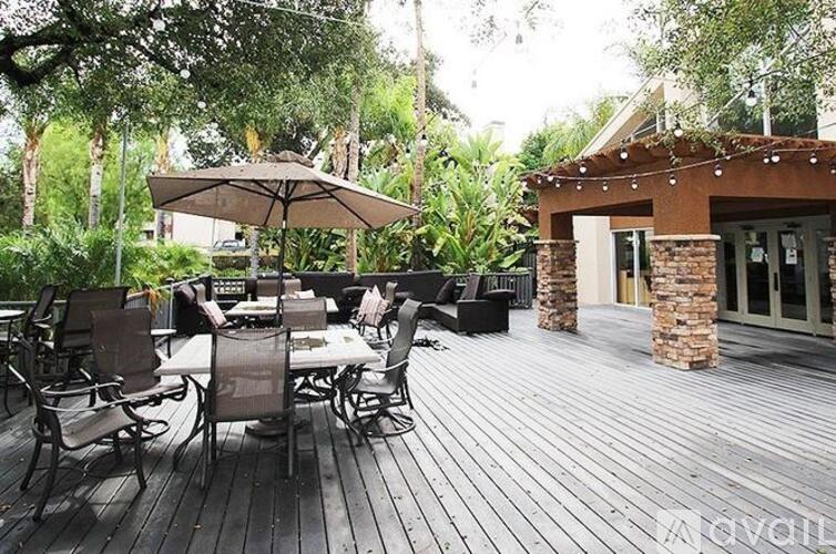 A wooden deck with chairs and an umbrella is surrounded by greenery.