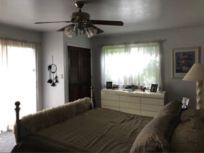 A bedroom with a bed, dresser, and a ceiling fan.