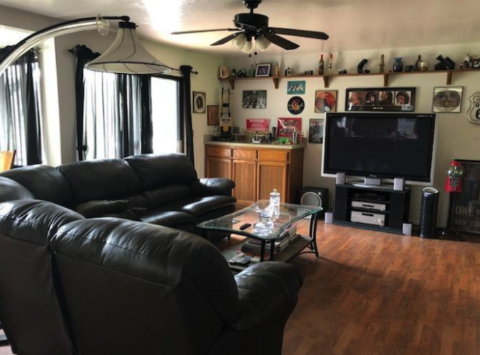 A black leather sofa sits in a living room with a ceiling fan and a television.