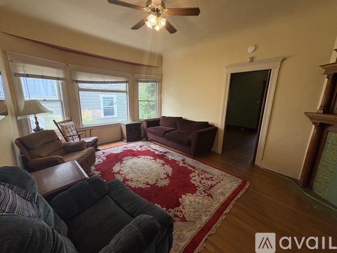 A living room with a rug, a couch, a chair, and a fan.