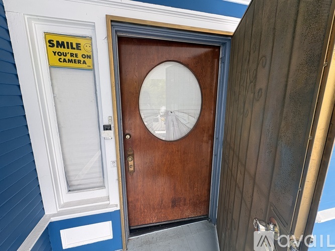 A brown door with a round window and a sign on the wall that says "Smile You're On Camera".