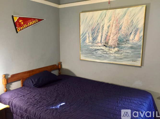 A bedroom with a bed and a painting of a sailboat on the wall.