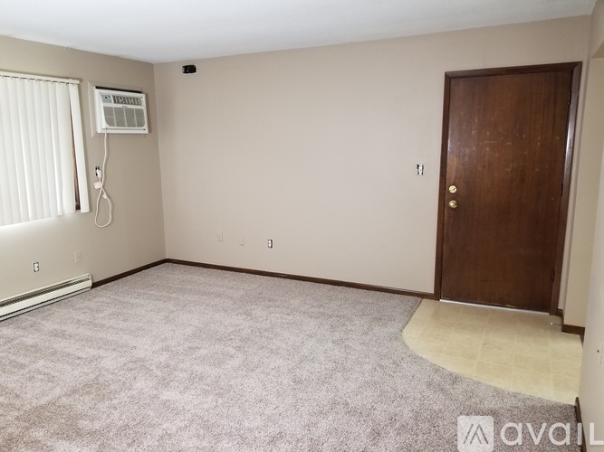 A room with a carpeted floor, a door, and a window with blinds.
