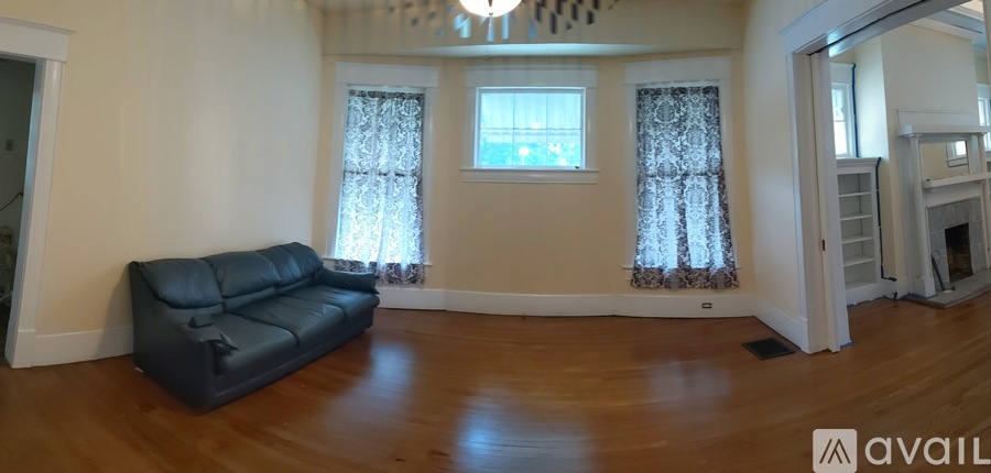 A black leather sofa sits in a spacious living room with hardwood floors and a chandelier.