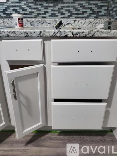 A white cabinet with a door is in front of a tiled wall.