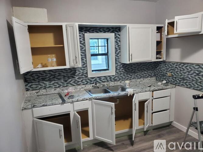 A kitchen with white cabinets and a granite countertop is under renovation.