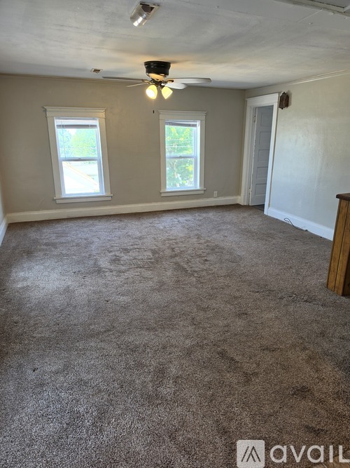 A room with a carpeted floor and two windows.