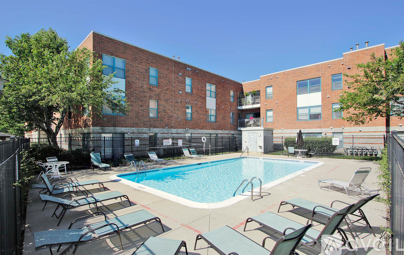 A pool surrounded by chairs and trees in front of a brick building.