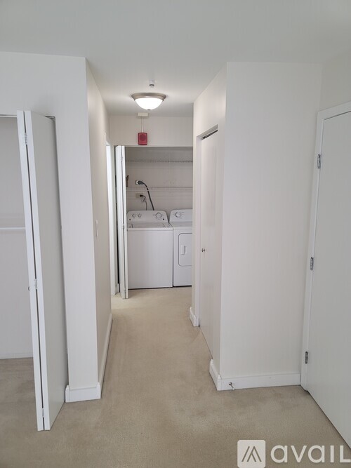 A white hallway with a door on the left and a laundry room in the distance.