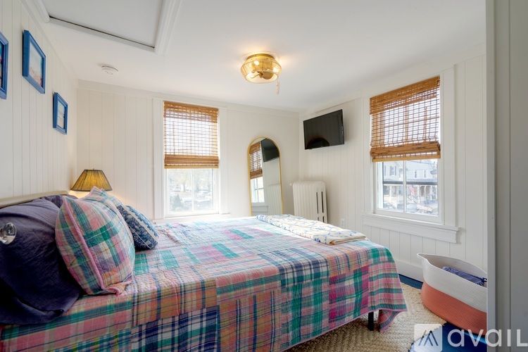 A bedroom with a bed covered in a plaid comforter and a flat screen TV mounted on the wall.