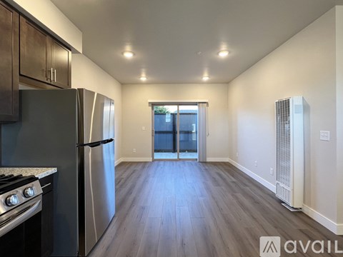 A kitchen with a stainless steel refrigerator and oven, wooden flooring, and a window with blinds.