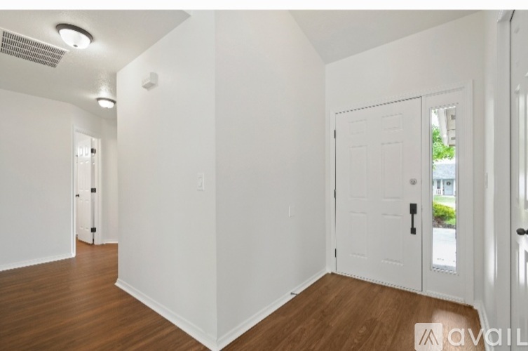 A room with white walls and wooden floors, with a door on the right side.