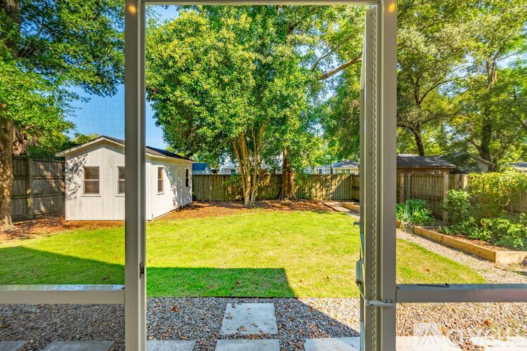 A view through a gate into a backyard with a lawn and trees.