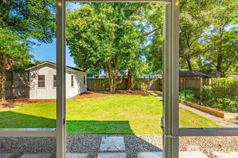 A view through a gate into a backyard with a lawn and trees.