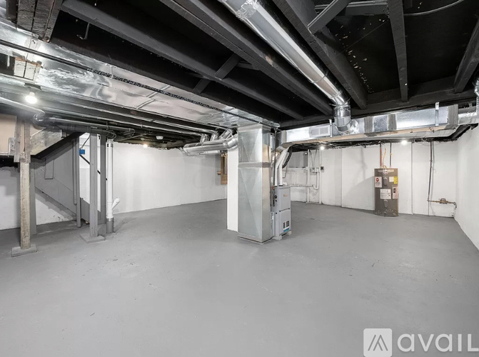 A large, empty industrial space with a concrete floor and exposed ceiling pipes.
