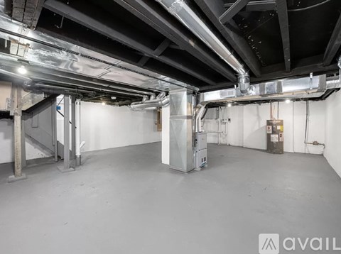 A large, empty industrial space with a concrete floor and exposed ceiling pipes.