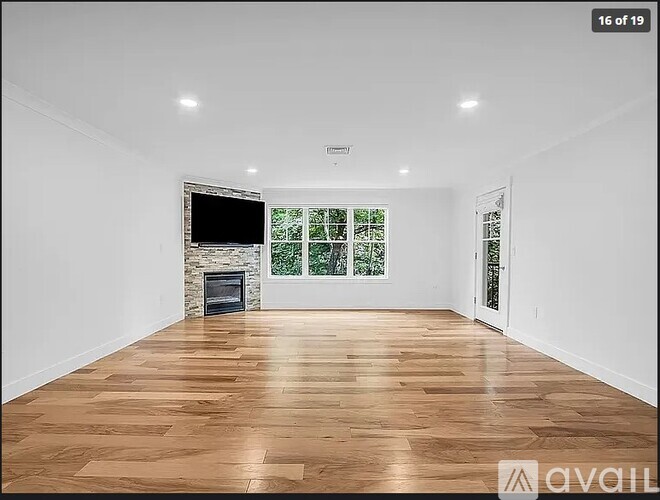 A spacious room with wooden flooring and a fireplace with a TV above it.