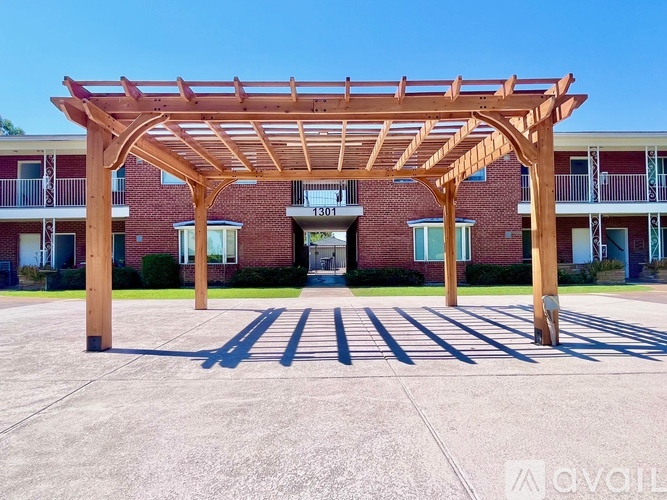 A wooden pergola is in front of a brick building with the number 1303 on it.