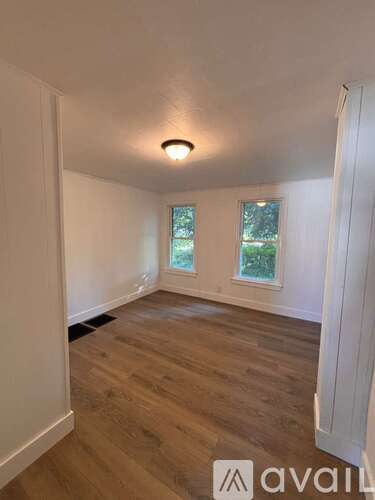 A room with wooden flooring and a window with a view of trees.