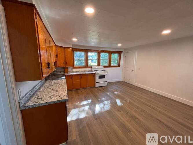 A spacious room with wooden floors and a kitchen area with cabinets and a countertop.