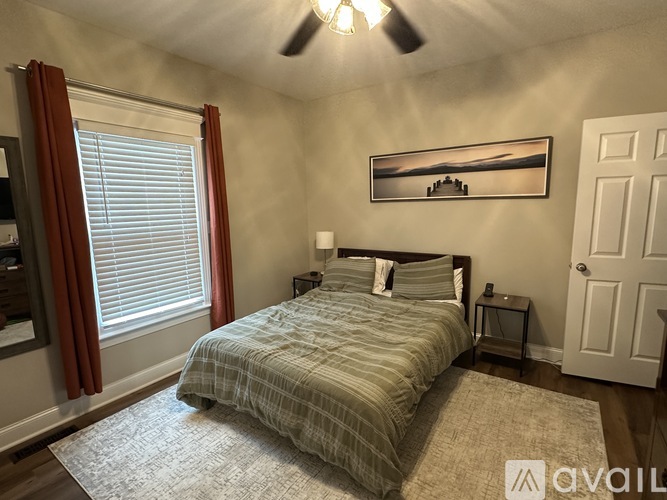 A bedroom with a bed, a ceiling fan, and a painting on the wall.