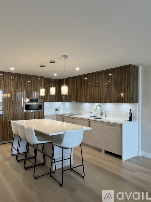 A modern kitchen with a large island and white chairs.