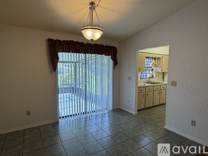 A room with a window covered by a red curtain and a sink in the kitchen area.