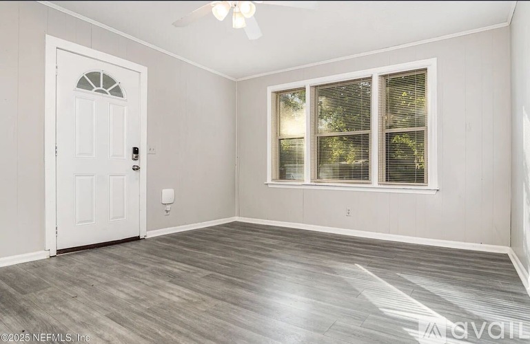 A room with a white door, a window with blinds, and a ceiling fan.