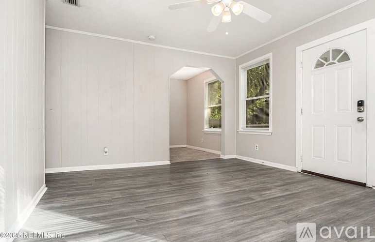 A spacious room with a white door and a ceiling fan.