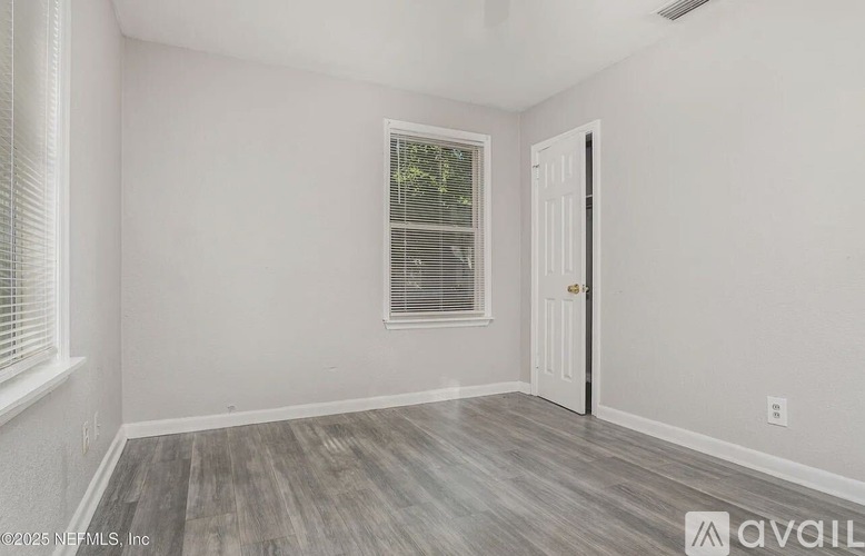 A room with a wooden floor, a window with blinds, and a door.