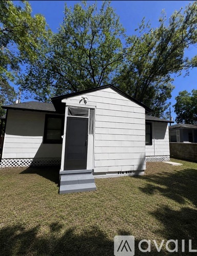A small white house with a black roof and a grey door is surrounded by a grassy area.