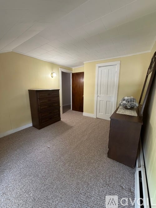 A hallway with a carpeted floor, a wooden cabinet, and a white door.